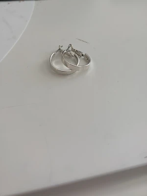 Silverfärgade hoop örhängen - Säljer ett par stilrena silverfärgade hoop örhängen med klassisk rund form. De är släta och har en enkel design som passar till många olika looks. Materialet ser ut att vara metall och de har ett smidigt lås. Perfekta för dig som gillar minimalistiska accessoarer. Från gekås Ullared.
