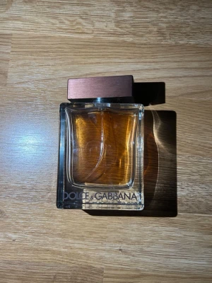 Dolce & Gabbana The One parfym - Säljer en Dolce & Gabbana The One parfym i en stilren, rektangulär glasflaska med bronsfärgat lock. Flaskan är genomskinlig och visar den gyllene vätskan inuti. Märkets logga syns tydligt på framsidan. Perfekt för dig som gillar exklusiva dofter.