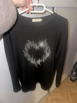 Svart tröja med glittrigt hjärta - Cool svart långärmad tröja från JansuMan med ett hjärtmotiv i silverdiamanter på bröstet. Storlek L men passar M också 