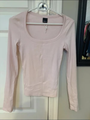 Ljusrosa långärmad topp Gina Tricot - Söt ljusrosa långärmad topp från Gina Tricot med rundad, djup ringning. Enkel och stilren design i mjuk bomullskvalitet. Perfekt att matcha med jeans eller kjol för en clean look.