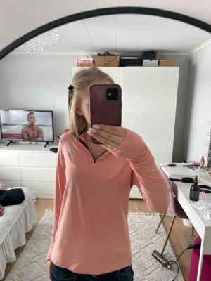 Ljusrosa långärmad tränings-topp - Ljusrosa långärmad tränings-topp med halv dragkedja framtill och diskret logga på bröstet. Materialet är mjukt och stretchigt, perfekt för sport och träning. Snygg passform och tumhål i ärmsluten för extra komfort.