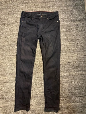 Mörkblå jeans från Tommy Hilfiger - Snygga mörkblå jeans från Tommy Hilfiger med klassisk femficksmodell och raka ben. Jeansen har diskreta sömmar och en liten logga på myntfickan. Tillverkade i ett mjukt och slitstarkt denimtyg som passar perfekt till din vardagsstil.