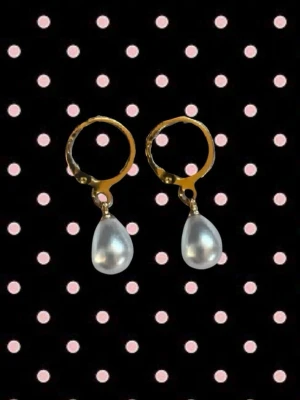 Guldörhängen med droppformade pärlor - Snygga örhängen med guldfärgade ringar och droppformade vita pärlor som hänger ned. Perfekt för dig som gillar klassisk stil med en modern twist.