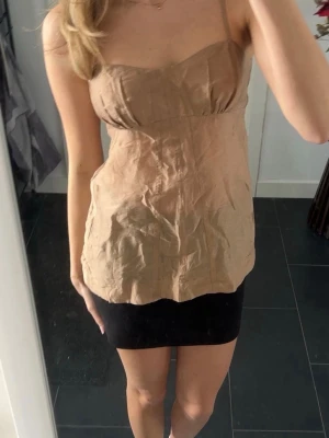 Beige linnetopp - Snygg beige linnetopp med smala axelband och figurnära passform. Toppen har en lätt rynkad byst och är perfekt för varma dagar. Enkel och stilren design som passar till mycket.