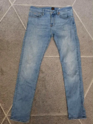 Ljusblå skinny jeans från Hugo Boss - Säljer ett par ljusblå skinny jeans från Nudie Jeans med klassisk femficksmodell och dragkedjegylf. Jeansen har en smal passform och är tillverkade i mjukt denimtyg. Perfekta för en avslappnad och trendig look.