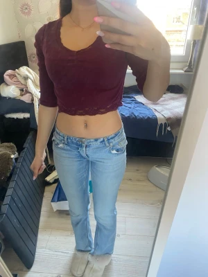 Vinröd croppad topp med spetskant - Säljer en vinröd croppad topp med v-ringning och spetskant. Toppen har trekvartsärm och är i ett ribbat material som sitter tight. Perfekt för dig som gillar trendiga och feminina plagg.