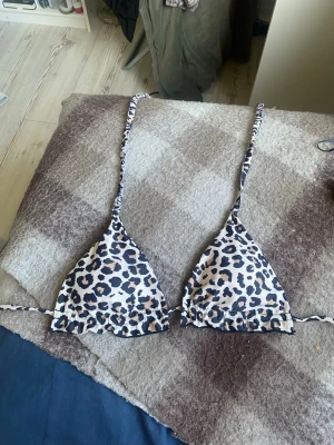 Leopardmönstrad trekantsbikini - Snygg trekantsbikini med leopardmönster i beige, svart och vitt. Bikinin har smala knytband i nacken och ryggen för justerbar passform. Perfekt för strandhäng eller poolparty.