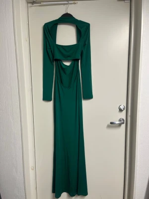 Grön långklänning med öppen rygg - Snygg grön långklänning i stretchigt material med lång ärm och öppen rygg. Klänningen har en unik cut-out detalj framtill och sitter tight längs kroppen för en smickrande siluett. Perfekt för dig som vill sticka ut med en elegant och modern look.