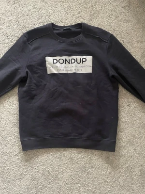 Mörk sweatshirt från Dondup - Cool svart sweatshirt från Dondup med stor vit logga och text på bröstet. Klassisk rund halsringning och ribbade muddar vid ärmslut och nederkant. Perfekt för en avslappnad och trendig look.