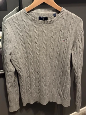 Grå kabelstickad tröja från Gant - Snygg grå kabelstickad tröja från Gant i premium bomull. Storlek M men sitter som S. Skriv vid frågor eller funderingar! 