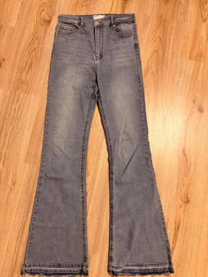 Blåa utsvängda jeans  - Snygga blå jeans med utsvängda ben och råa kanter nertill. Klassisk femficksmodell med hög midja och dragkedja. Perfekta för dig som gillar en retroinspirerad look och vill sticka ut lite extra.