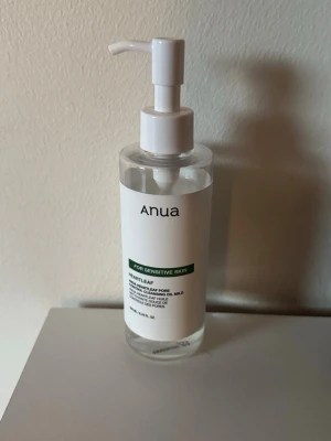 Anua Heartleaf Cleansing Oil - Mild rengöringsolja från Anua med pumpflaska, speciellt framtagen för känslig hud. Transparent olja i en genomskinlig plastflaska med vit etikett och grön text. Perfekt för att ta bort smink och rengöra porer.