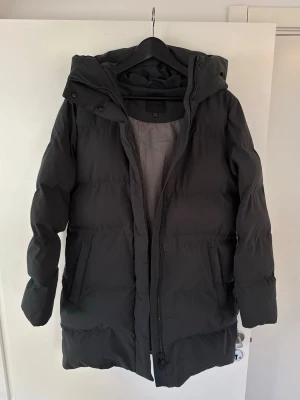 Mörkgrön lång pufferjacka från ELVINE - Säljer min fina och varma vinterjacka från det svenska märket ELVINE і storlek XS. Passar även till S och M.  Jackan är i en snygg mörkgrön färg med en rejäl huva som skyddar bra mot kyla och vind. Den är använd under två säsonger men är väl omhändertagen och fortfarande i mycket gott skick.  Säljer den nu då den tyvärr har blivit för liten för mig. Det är en klassisk och stilren modell med hög kvalitet som passar till det mesta.  Hör gärna av dig om du har några frågor eller vill ha fler bilder