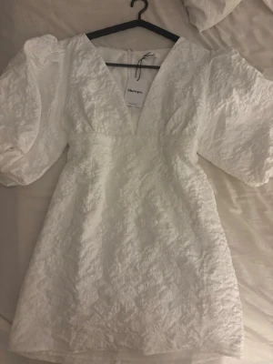 Vit kort klänning från Showpo - Är i XL men jag som använder M passar den perfekt .Supersnygg vit kort klänning från Showpo med puffiga ärmar och djup v-ringning. Klänningen har ett strukturerat tyg med diskret mönster och dragkedja i ryggen. Perfekt för dig som vill sticka ut med en trendig och elegant look.