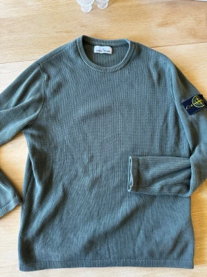 Grön stickad tröja från Stone Island - Snygg grön stickad tröja från Stone Island med klassisk rund halsringning och ikonisk logotyp-patch på ärmen. Tröjan har ribbade muddar och är tillverkad i mjukt material som känns skönt mot huden.