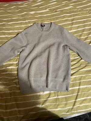 Ljusgrå stickad tröja från Uniqlo - En stilren ljusgrå stickad tröja från Uniqlo med rund halsringning och ribbade muddar vid ärmslut och nederkant. Perfekt basplagg för lager på lager och enkel att matcha med olika outfits. Tillverkad i mjukt material för skön känsla. Endast använd ett par gånger. Tröjan är i storlek S, priset är 150. Hojta till om du vill se fler bilder! 