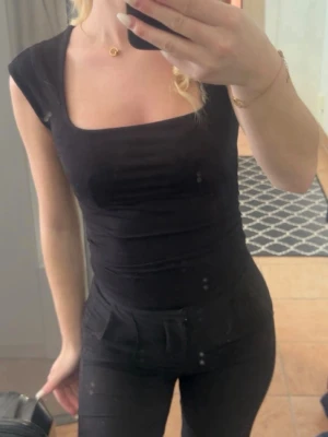 Svart  linnetopp med fyrkantig ringning - Snygg svart linnetopp med fyrkantig ringning och breda axelband. Toppen är tight i modellen och har en enkel, stilren look som passar till det mesta.