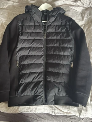 Svart cardigan med dragkedja - Svart hoodie med quiltad framsida i vadderad polyester och mjuka ärmar samt rygg i bomullsmix. Tröjan har huva, två sidofickor med dragkedja och ribbade muddar. Perfekt för lager på lager och streetwear-vibe. Från italia by versace 19v69