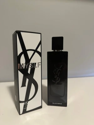 YSL MYSLF Eau de Parfum - YSL MYSLF Eau de Parfum med elegant svart rektangulär flaska och matchande svart lock. Flaskan har en stilren design med YSL-loggan i silver och kommer i en snygg svartvit kartong. Perfekt för dig som gillar exklusiva och moderna dofter.