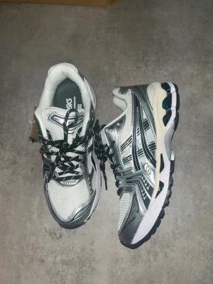 Asics silvervita sneakers - Pris kan diskuteras. Helt nya med prislapp för små för mina fötter.Snygga sneakers från Asics i silver och vitt med svarta detaljer. Skorna har mesh-tyg för bra ventilation och reflekterande partier. Klassisk låg modell med svartvita snören och bekväm sula som ger bra stöd. Perfekta för dig som gillar sportig stil.