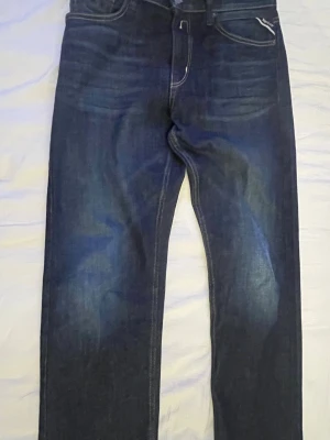 Mörkblå replay jeans  - Snygga mörkblå i storlek XS i vuxen storlek jeans med raka ben och kontrastsömmar. Jeansen har klassisk femficksdesign, diskreta slitningar framtill och detaljerade bakfickor. Perfekta för en avslappnad och stilren look.