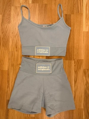 Ljusblått set från Adidas Originals topp shorts träning - Snyggt ljusblått träningsset från Adidas Originals med crop top och höga shorts. Båda delarna har bred resår med Adidas-logga framtill. Tillverkat i mjukt material, perfekt för gymmet eller danspasset. Smala axelband på toppen och bekväm passform. Storlek XS. Använt en gång.