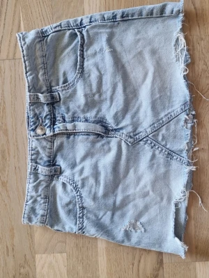 Ljusblå jeanskjol med rå kant - Säljer en ljusblå jeanskjol med fransig kant och slitningar framtill. Kjolen har klassiska fem fickor, bälteshällor och snygga bakfickor med broderade detaljer. I strl 170. Använd ca 3 gånger