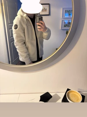 Napapijri teddyjacka - Mysig beige teddyjacka från Napapijri med dragkedja, huva och två stora fickor framtill. Jackan har en patch med logga på ena ärmen och är tillverkad i fluffigt teddy-material som håller dig varm och bekväm. Nypris 3000kr, använd 4-5 gånger