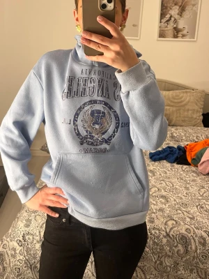Ljusblå hoodie från SHEIN - Ljusblå hoodie från SHEIN med tryck framtill som säger 'Los Angeles' och har en cool emblem-design. Hoodien har stor känguruficka, ribbade muddar och mjukt fleecefoder på insidan. Perfekt för en chill och avslappnad stil.