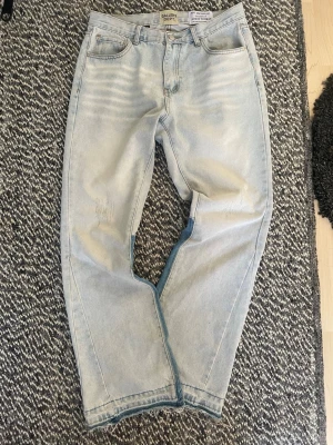 Ljusblå jeans från Gallery Dept - Unika ljusblå jeans från Gallery Dept med raka ben och cool patchwork-detalj i mörkare denim på insidan av benen. Jeansen har fem fickor, fransade benslut och klassisk knappgylf. Perfekta för dig som vill sticka ut med en kreativ och trendig look.