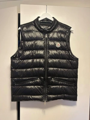 Moncler gui väst - Snygg svart dunväst från Moncler storlek 2 (S/M) med glansig finish, ståkrage och två dragkedjefickor framtill.Det är en 1:1 guiväst utan någon skada på den. Västen har Moncler-logga på bröstet och stängs med en robust dragkedja. Perfekt för lager-på-lager. Är du intresserad eller har några frågor är de bara att fråga.