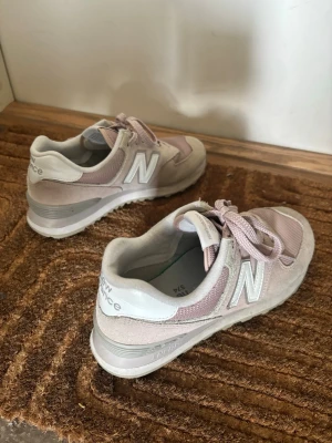 Ljusrosa New Balance sneakers - Säljer ett par ljusrosa New Balance sneakers med vita och grå detaljer. Skorna har klassisk mesh och mocka på ovandelen, snörning och den ikoniska N-loggan på sidan. Perfekta för dig som gillar sportig och stilren look.