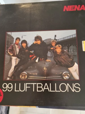 Nena 99 Luftballons LP - LP Nena-albumet med låten 99 Luftballons. Omslaget är svart med ett foto av bandet framför en bil och tydlig vit text. Baksidan har en mindre svartvit bild och information om albumet. Perfekt för dig som gillar 80-talsmusik och samlar på vinylrelaterade böcker.Inga repor.