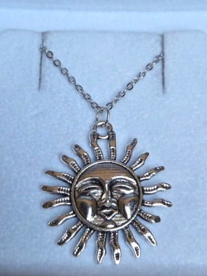 Silvrigt solformat halsband rostfritt stål  - Unikt halsband med ett solformat hänge i silverfärgad metall. Hänget har detaljerade, vågiga solstrålar och hänger på en tunn kedja. Perfekt accessoar för dig som gillar statement-smycken och vill sticka ut med en cool design. Hänget är ca 3 cm och kedjan 45 cm.