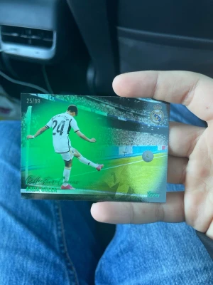 Arda Güler Real Madrid samlarkort - Unikt samlarkort från Topps med Arda Güler i Real Madrid, numrerat 25/99. Kortet har en grön och svart design med spelaren i matchställ och Real Madrids logga. Perfekt för dig som gillar fotboll och samlar på sportkort. 25/99 innebär att det endast finns 99 kort av detta kortet
