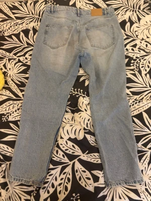 Ljusblå raka jeans i klassisk modell - Säljer ett par ljusblå jeans med rak passform och hög midja. Jeansen har fem fickor och bälteshällor, tillverkade i klassisk denim. Perfekta för en avslappnad och trendig look.