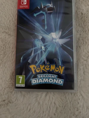 Pokémon Brilliant Diamond Switch - Pokémon Brilliant Diamond till Nintendo Switch. Omslaget är svart och blått med legendariska Pokémon Dialga i centrum. Spelet är i fysisk kassettform och har PEGI 7-märkning. Perfekt för dig som gillar äventyr och att samla Pokémon.
