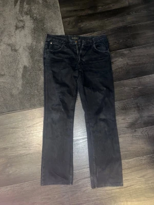 Svarta raka jeans från Valentino - Säljer ett par svarta jeans från Valentino med rak passform och klassisk femficksdesign. Jeansen har guldfärgade detaljer och är tillverkade i ett slitstarkt denimtyg. Perfekta för dig som vill ha en stilren och tidlös look.