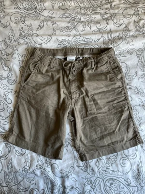 Khaki shorts med snörning från Jack & Jones - Snygga beige shorts från Jack & Jones med snörning i midjan och avslappnad passform. Tillverkade i mjuk bomull, perfekta för varma dagar. Två fickor fram och två bakfickor för en klassisk look.
