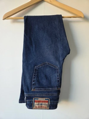 Blå bootcut jeans från Diesel - Snygga blå bootcut jeans från Diesel med klassisk femficksdesign och tydlig logga på bakfickan. Jeansen har en något utsvängd passform och är tillverkade i slitstark denim. Perfekta för dig som gillar en tidlös och cool stil. Storlek 27 W L. 32