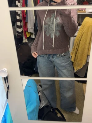 Lila stickad hoodie med mönster - Säljer en lila stickad hoodie med ljusgrått snöre och ett stort grafiskt mönster framtill. Tröjan har långa ärmar, ribbade muddar och en mysig huva. Perfekt för dig som gillar en avslappnad och cool stil.