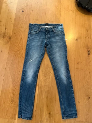 Blå slim fit jeans från Solid - Snygga blå slim fit jeans från Solid med klassisk femficksdesign och lätt slitna detaljer på benen. Jeansen har normal midja och raka ben.