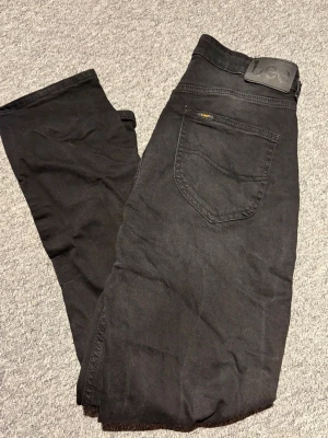 Svarta jeans från Lee - Säljer ett par svarta jeans från Lee med klassisk femficksdesign och rak passform. Jeansen har en diskret Lee-logga på bakfickan och är tillverkade i ett mjukt bomullsmaterial med lite stretch för extra komfort. Perfekta till din vardagsstil!