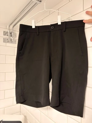 Svarta Les Deux kostym shorts - Stilrena svarta ”kostym” shorts med normal passform, bälteshällor och knapp framtill. Shortsen har två sidofickor och två bakfickor, perfekt för en clean och enkel look. 