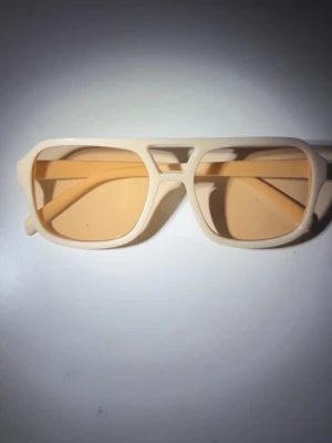 Beige retro solglasögon - Snygga solglasögon i retrostil med beige bågar och ljusbruna glas. De har en unik, kantig form och bred brygga som ger en cool vintagekänsla. Perfekta för dig som vill sticka ut med en stilren accessoar.
