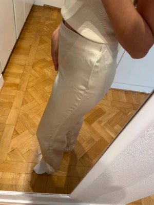 Vida beige satinbyxor  - Snygga beige satinbyxor med hög midja och raka, vida ben. Byxorna har en clean look utan synliga fickor eller detaljer och är tillverkade i ett lätt och luftigt material. Köpta från Zara och aldrig använda.