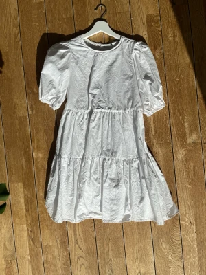 Vit kort klänning från Zara - Superfin vit kort klänning från Zara med puffärmar och öppen rygg. Klänningen har volangdetaljer och knyt i ryggen, vilket ger en söt och trendig look. Perfekt för varma dagar och somriga vibes.