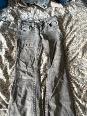 Grå bootcut jeans med fickdetaljer - Snygga grå jeans med bootcut passform och klassiska fem fickor. Jeansen har coola sömdetaljer och ficklock bak. Perfekta för en avslappnad och trendig look. Materialet är denim med lätt stretch för extra komfort.