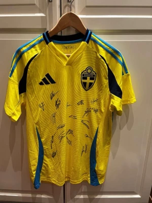 Signerad Sverige Matchtröja Herrlandslaget 2025 - Oanvänd officiell Adidas Sverige-matchtröja med lappar kvar. Signerad av Sveriges herrlandslag 2025, vilket gör den till en unik samlarartikel för fotbollsfans. Sveriges emblem på bröstet, Adidas-logotyp framtill och “SVERIGE” tryckt i nacken. AEROREADY-material för hög komfort. Nypris utan autografer: 1 199 kr. Perfekt för samlare eller supporter.
