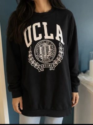 Svart UCLA sweatshirt med tryck strl S - Svart oversized sweatshirt  UCLA med stort vitt tryck framtill. Tröjan har rund halsringning, långa ärmar och ribbade muddar vid ärmslut och nederkant. Materialet är mjukt och bekvämt, perfekt för en avslappnad stil.